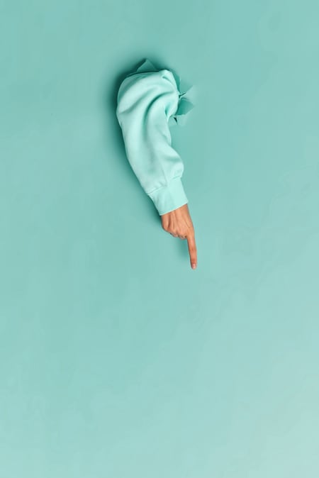 woman-hand-blue-sweater-breaking-through-paper-wall-pointing-copy-space