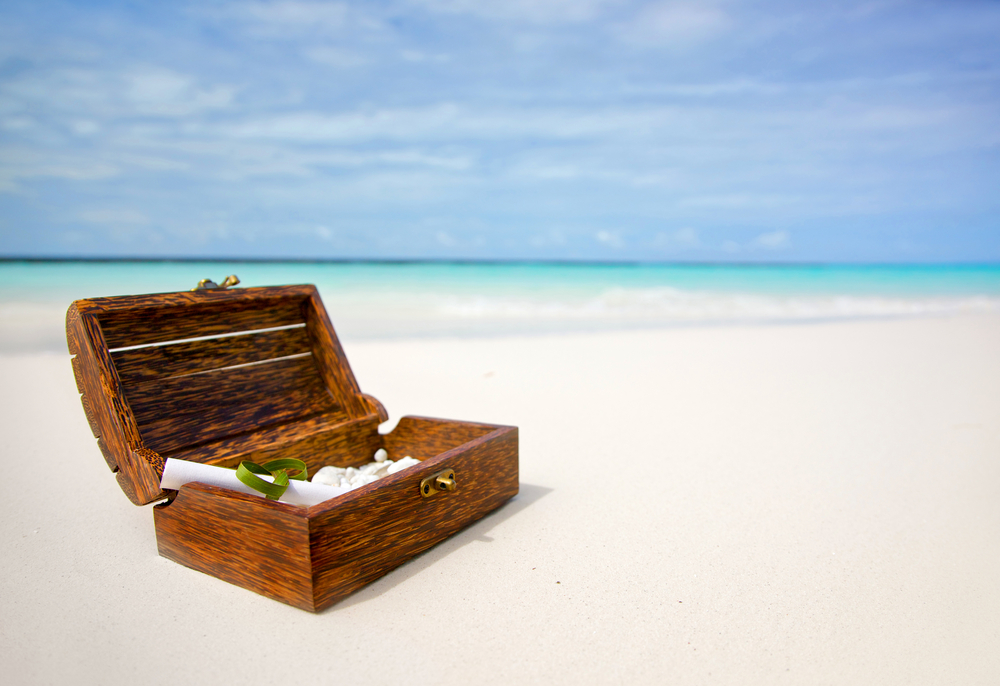 Treasure chest on white sand. Blue sea in background 