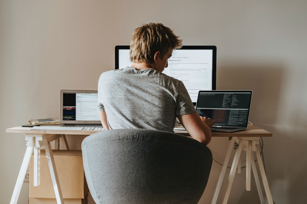 Man working from home looking at three computer screens
