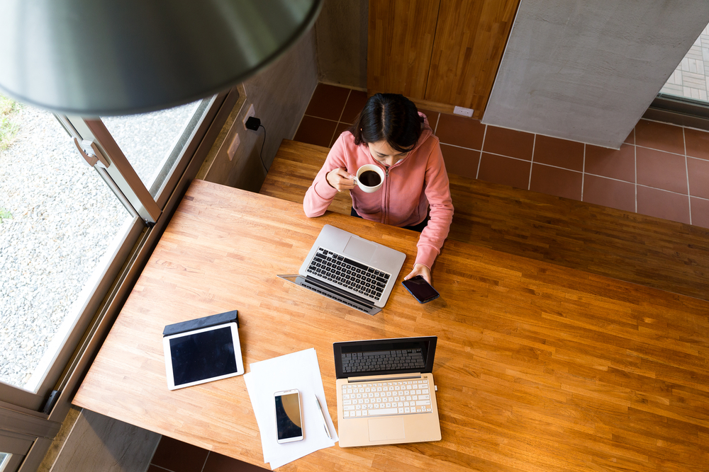 Top view of woman drinking of coffee with checking the message on cellphone while hybrid working